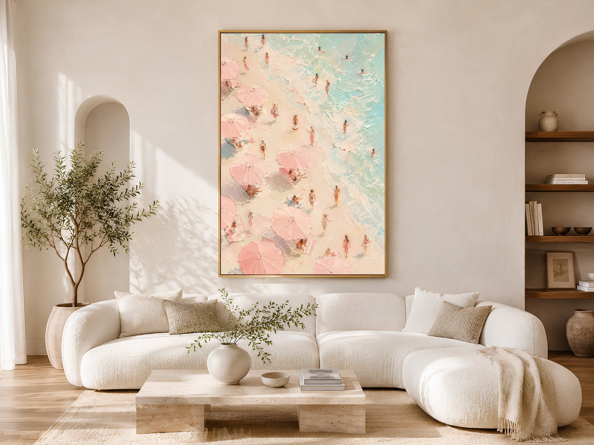 Pink beach figures wall art in gold frame above a cream sofa in a bright neutral living room with arched shelving