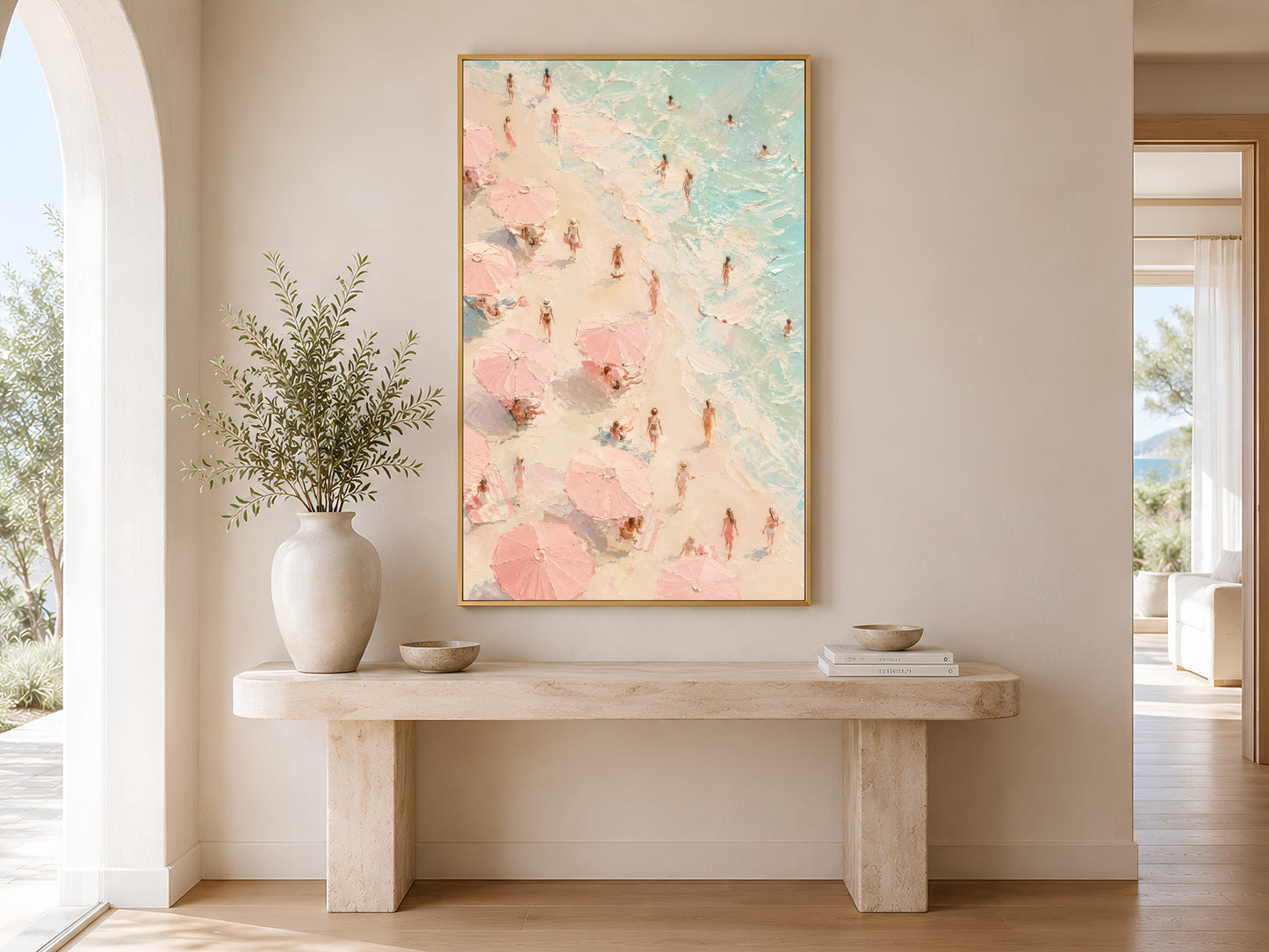 Pink aerial beach scene print in gold frame above a console table in a minimal bright neutral hallway
