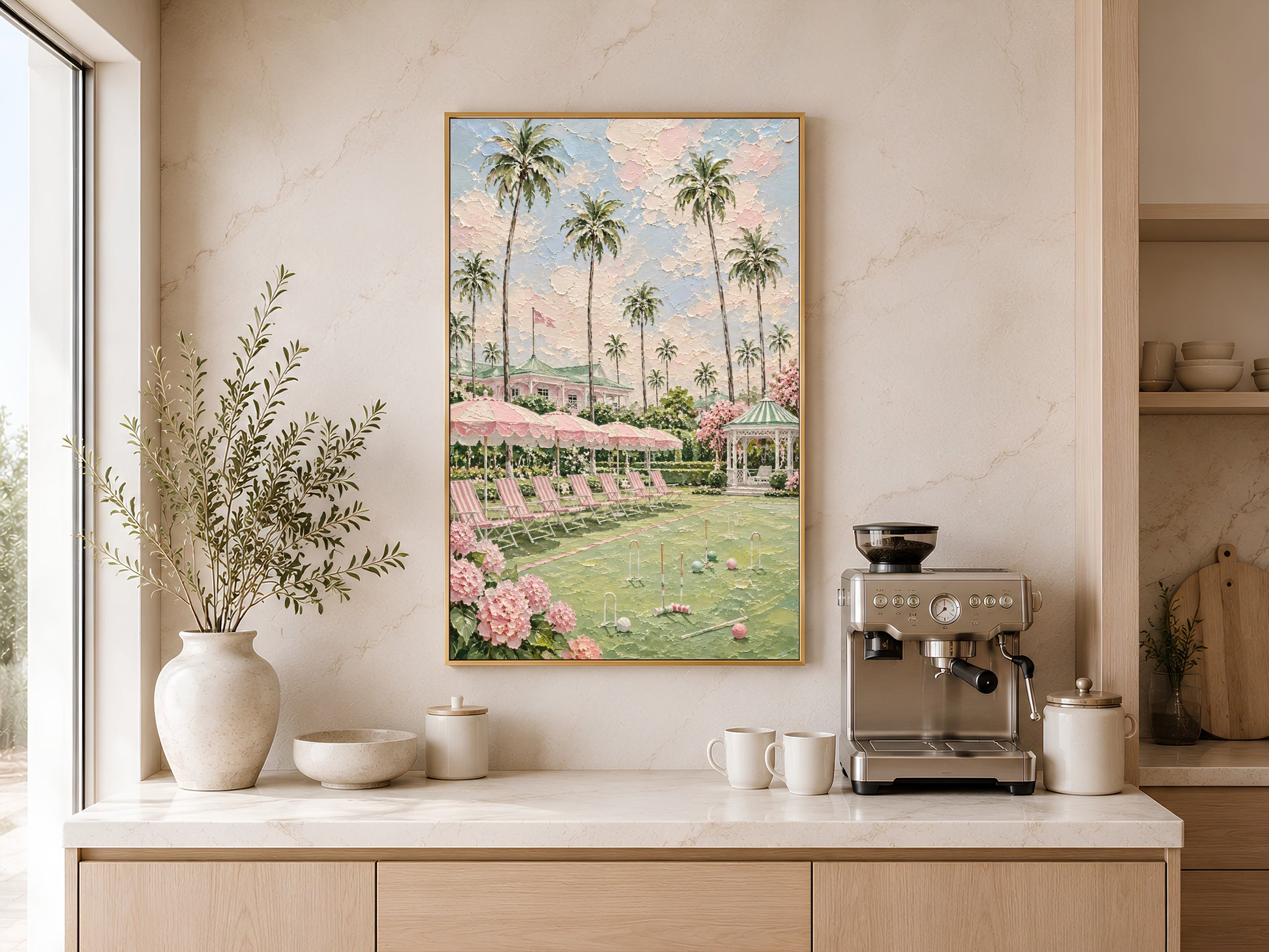 Gold-framed country club croquet lawn wall art above a light wood kitchen counter with a coffee station, neutral cabinetry, and a large round white vase
