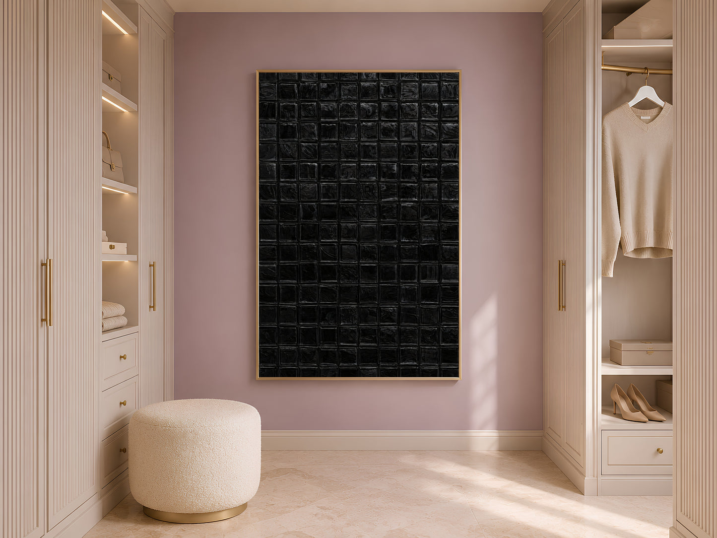 Black mosaic tile wall art in a gold frame hanging in a bright walk-in closet with cream shelving, warm oak floor, and a round boucle ottoman
