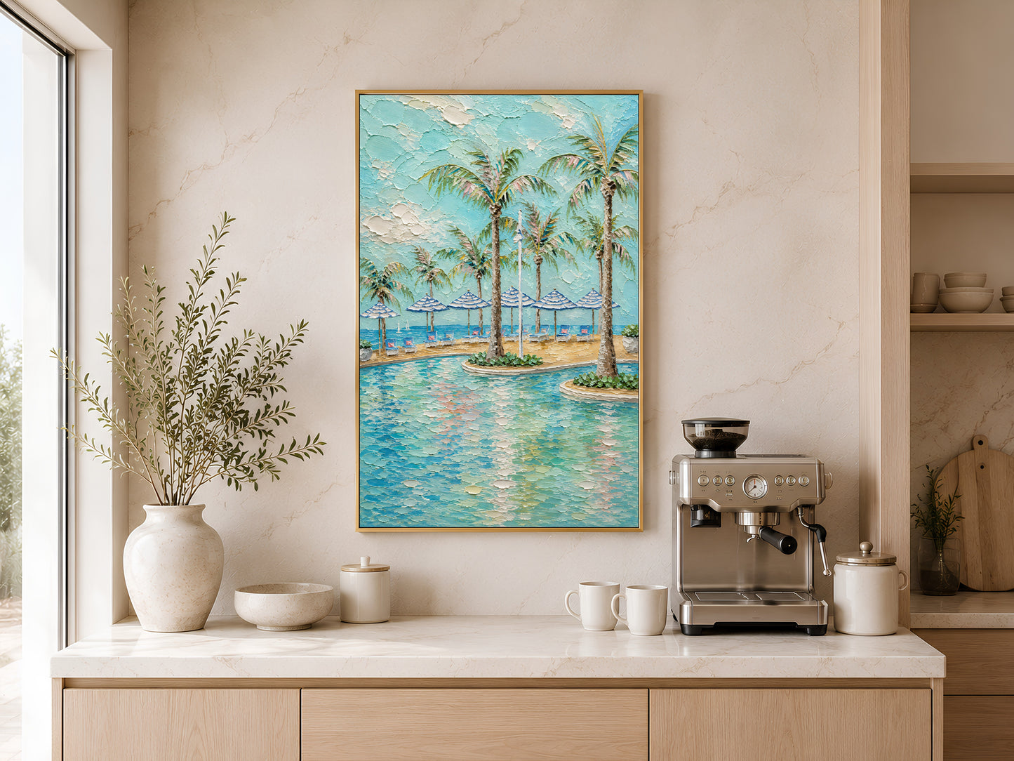 Gold-framed tropical beach club wall art above a light wood kitchen counter with a coffee station, neutral cabinetry, and a large round white vase with greenery
