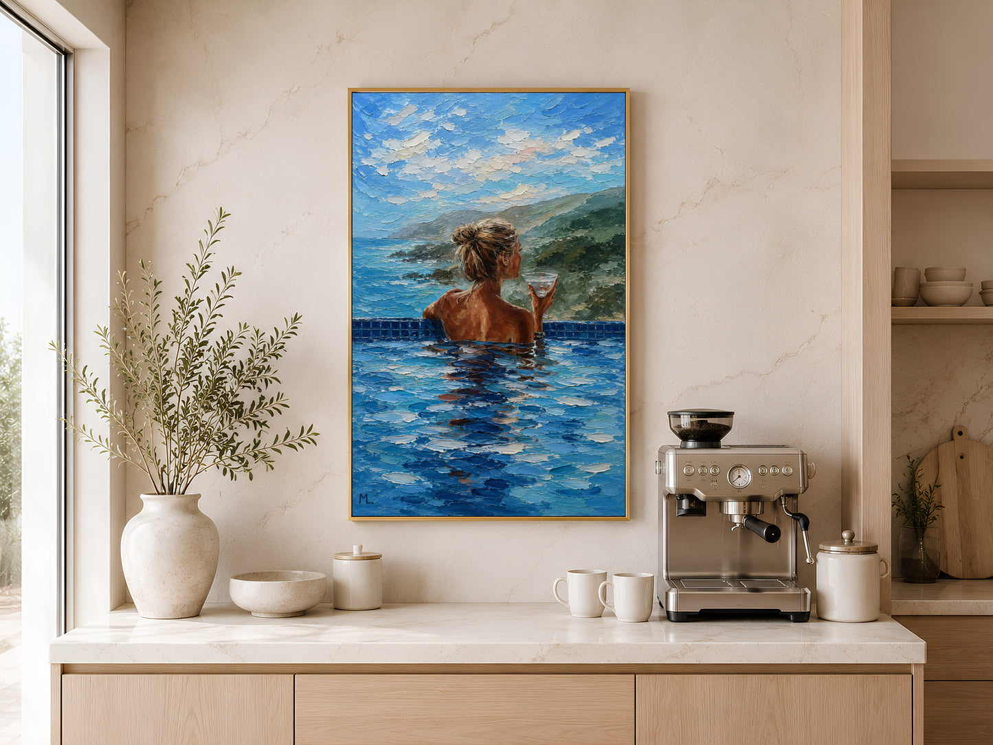Gold-framed woman in infinity pool coastal view wall art above a light wood kitchen counter with a coffee station and a large round ceramic vase
