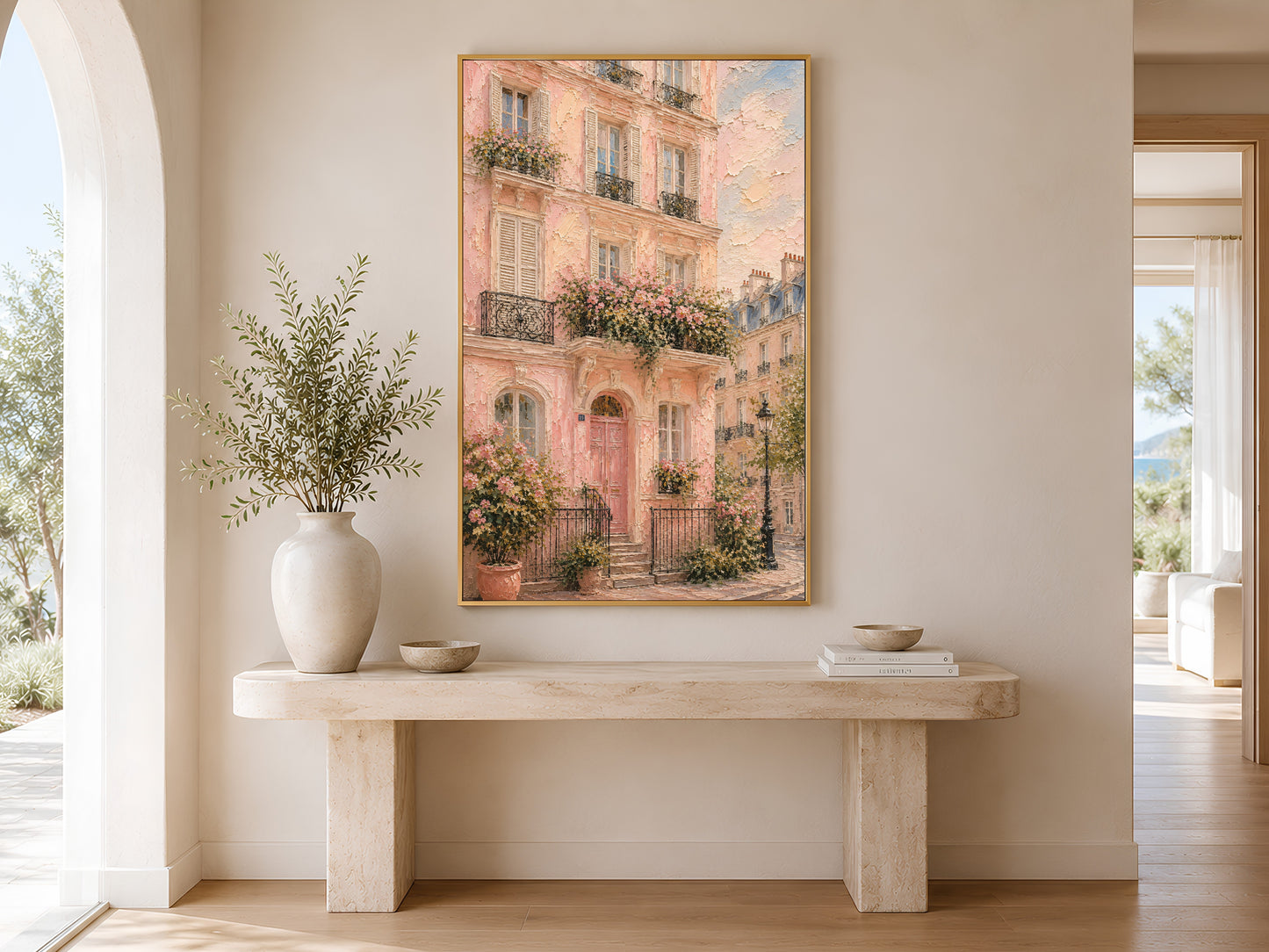 Framed pink Parisian building wall art in a gold frame on a warm white wall in a bright minimal entryway with cream console table and olive stems
