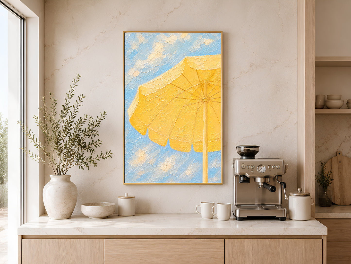 Framed yellow beach umbrella painting print on a warm white wall above a kitchen sideboard with ceramic vases and coffee machine
