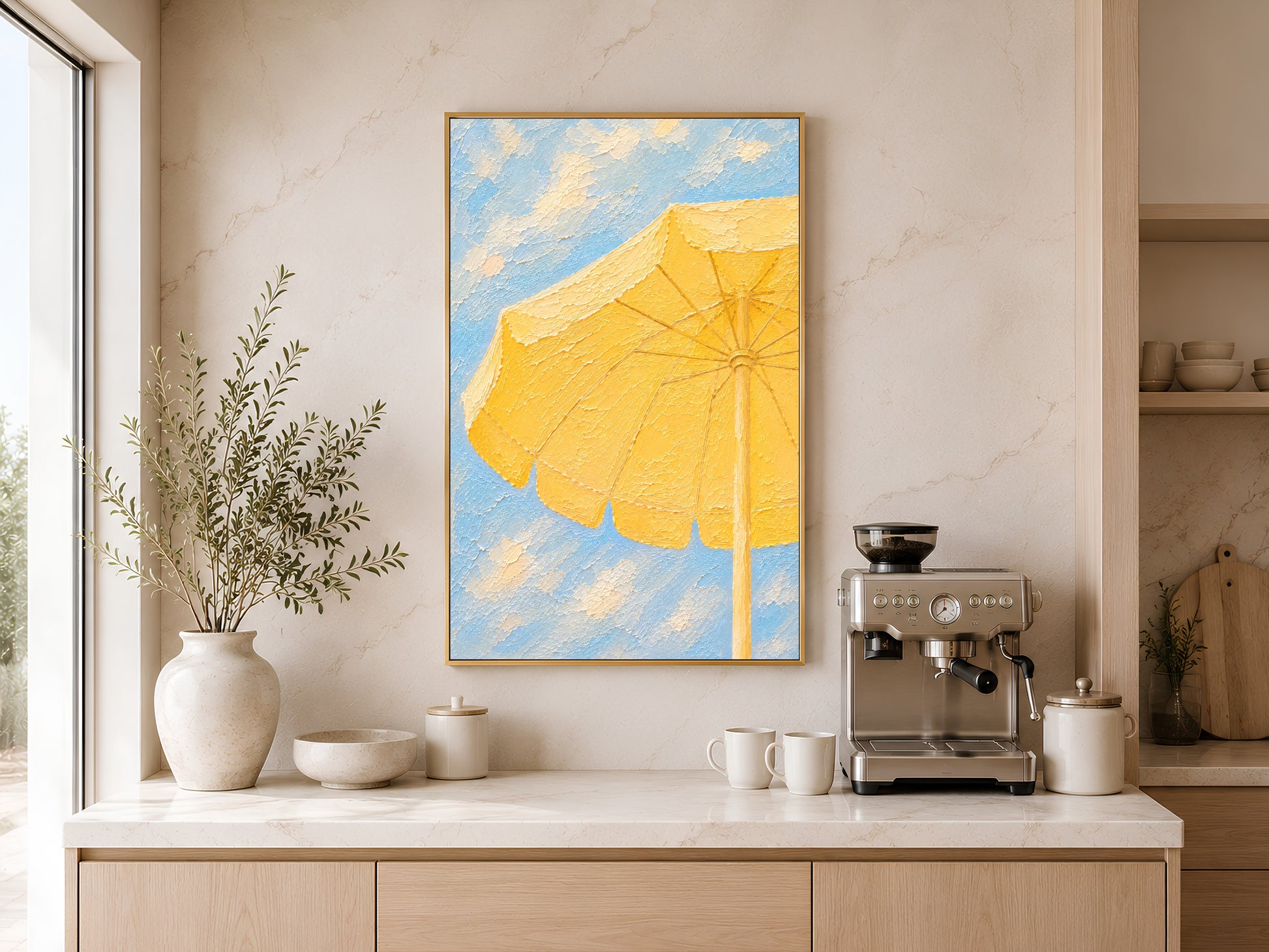 Framed yellow beach umbrella painting print on a warm white wall above a kitchen sideboard with ceramic vases and coffee machine
