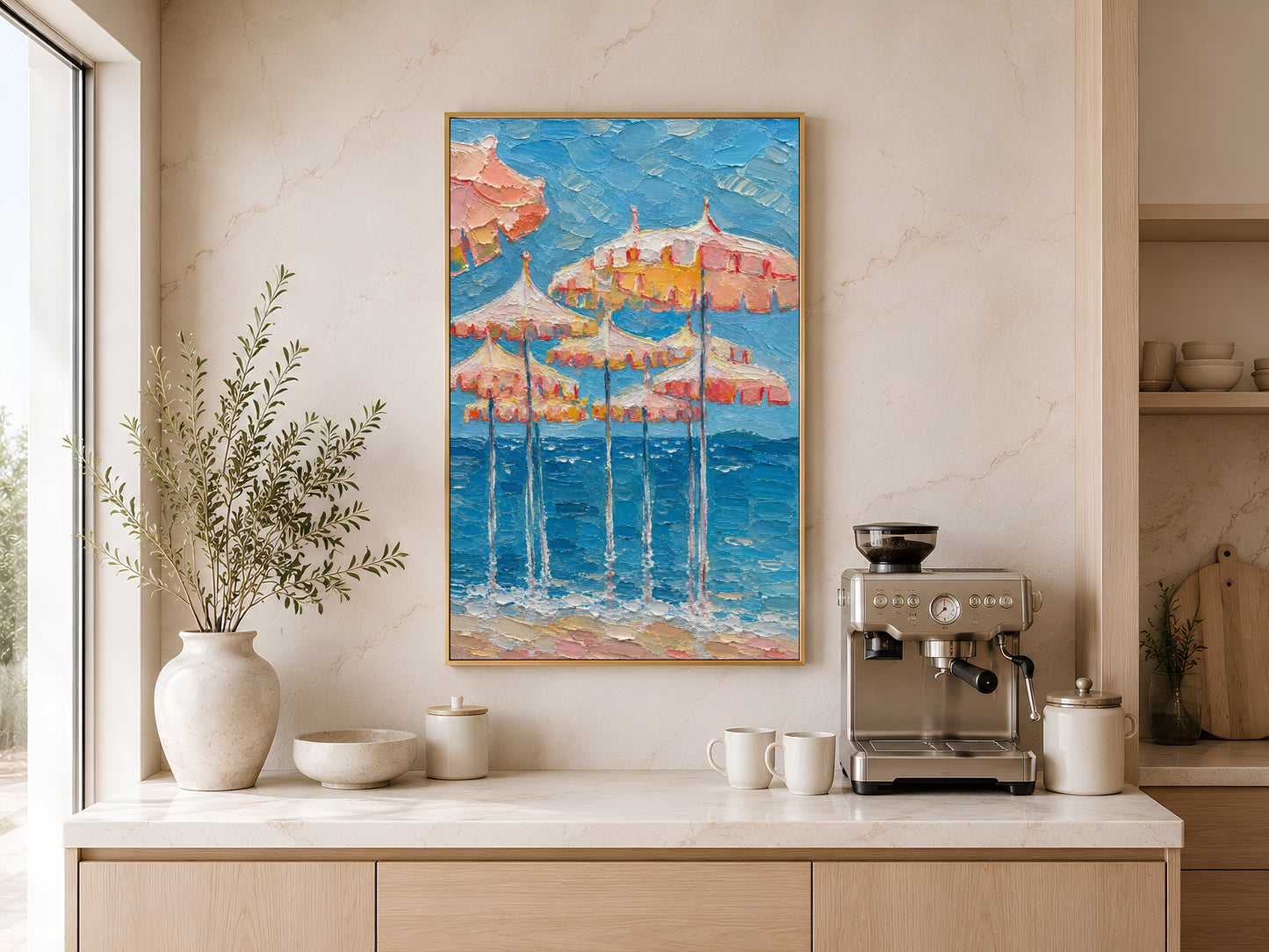 Gold-framed pink and peach beach umbrella wall art displayed above a kitchen counter with a coffee station and warm neutral cabinetry
