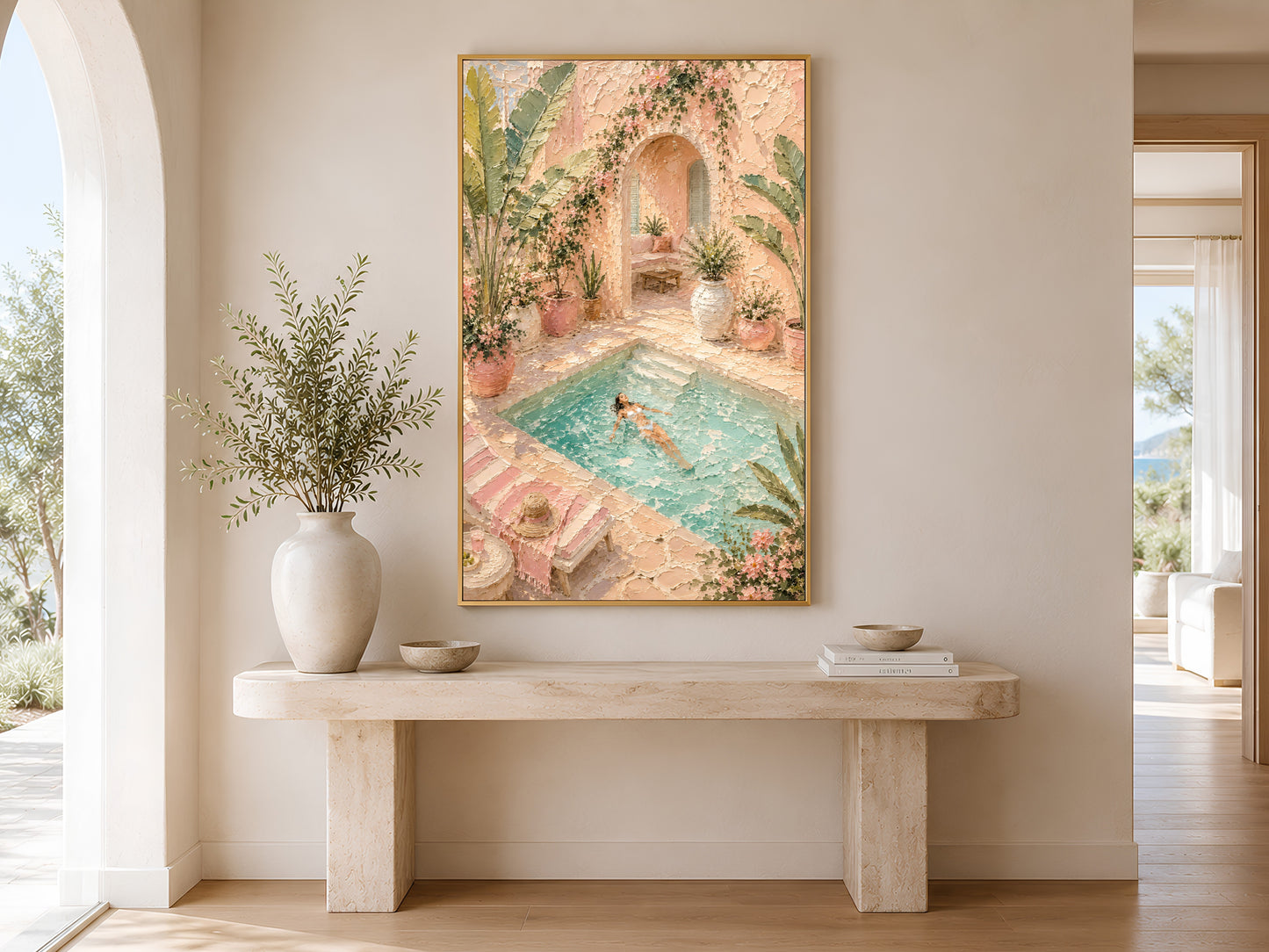 Framed pool villa impasto print in a gold frame in a bright minimalist entryway with cream console table, olive tree and arch doorway
