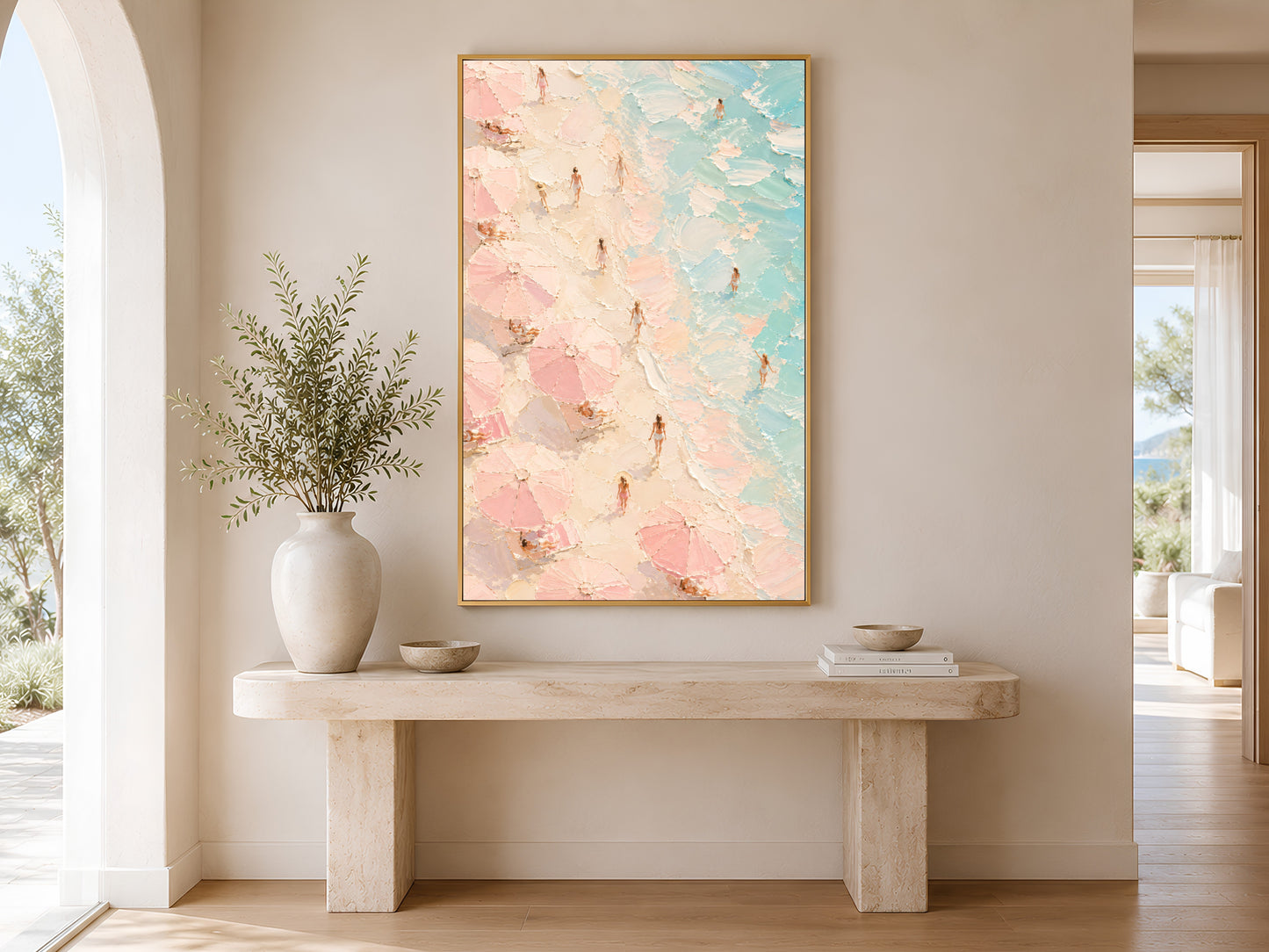 Framed aerial beach painting print in pink and teal hanging in a bright Scandinavian entryway with arched doorway and cream console table
