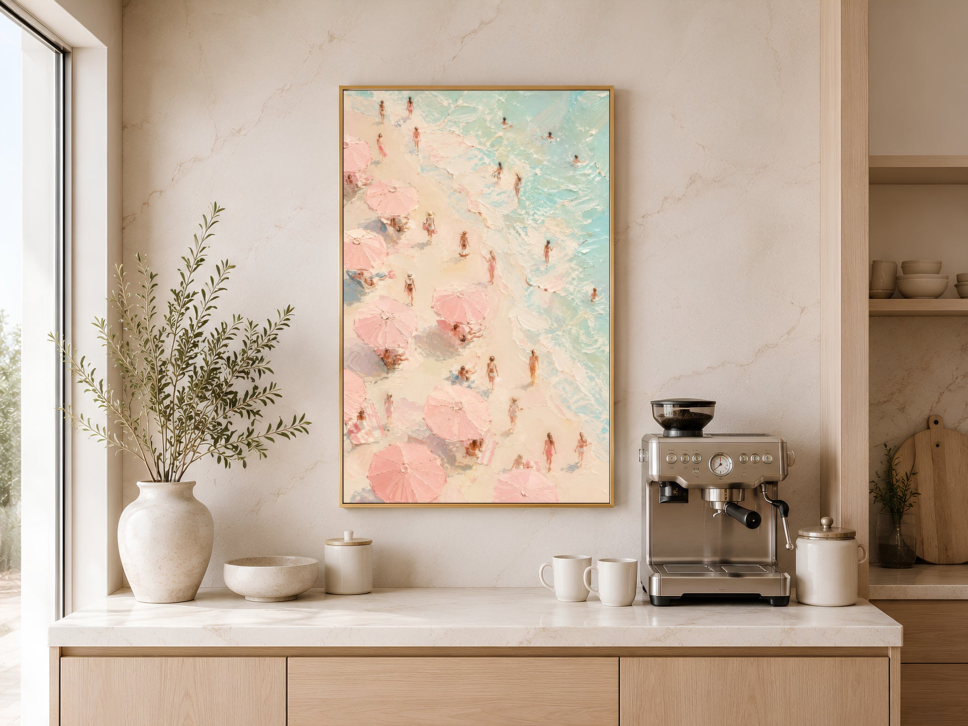 Aerial beach scene print in gold frame above a wooden sideboard with coffee machine in a warm neutral kitchen