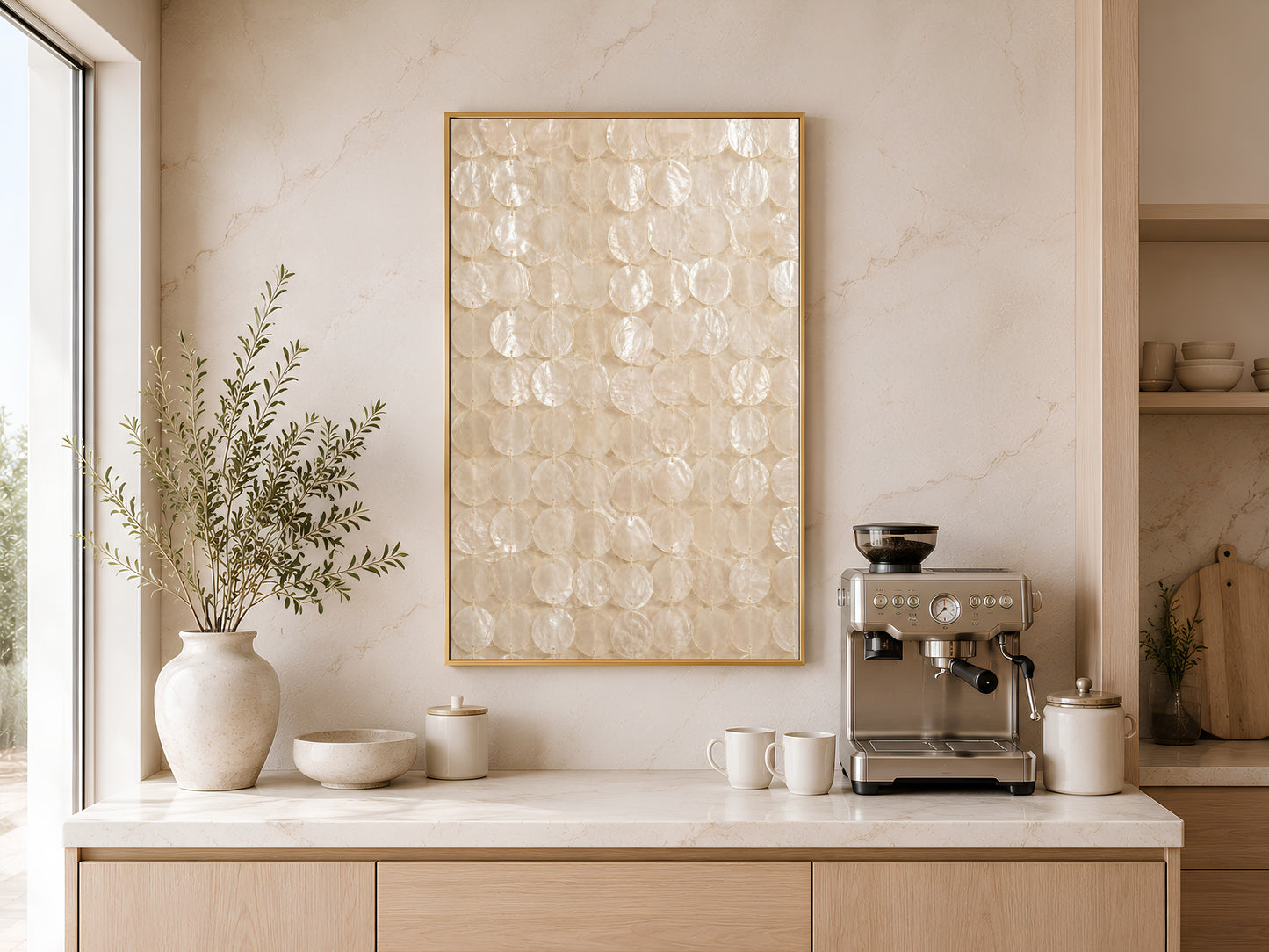 Capiz shell wall art print in a gold frame displayed above a light wood sideboard in a modern kitchen with neutral tones, neutral vases, pendant light, and warm natural light
