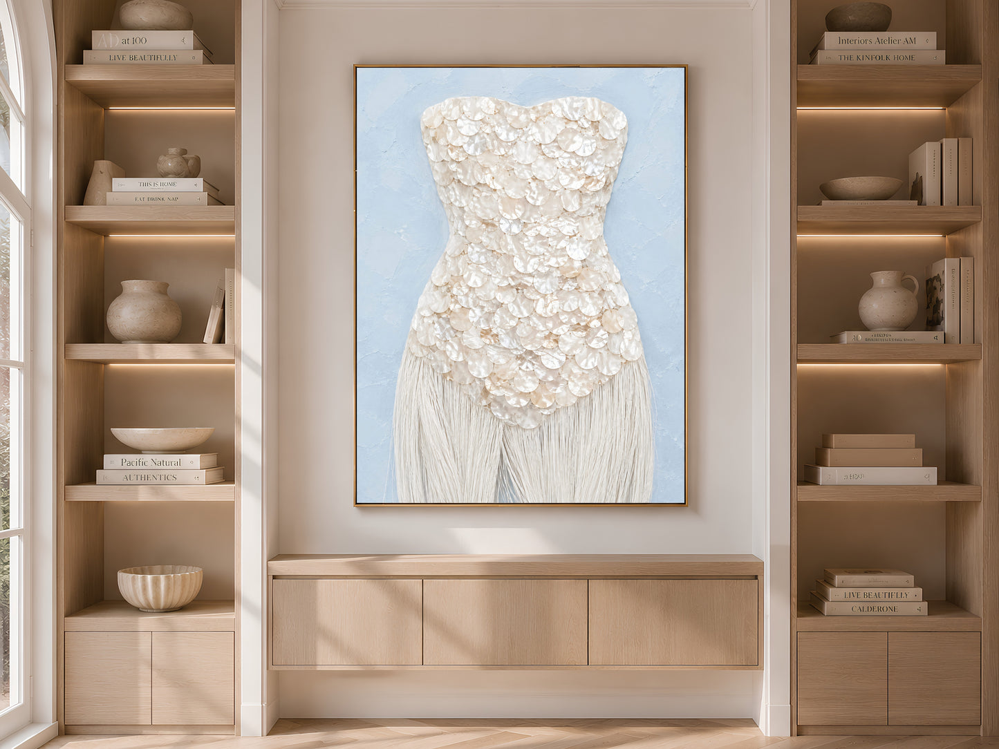 Coastal mother of pearl print in a gold frame displayed within light wood built-in shelving.