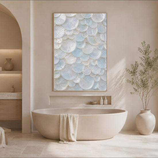 Sunlit bathroom with a freestanding tub, potted greenery, and a framed sea glass shell print above the vanity nook.